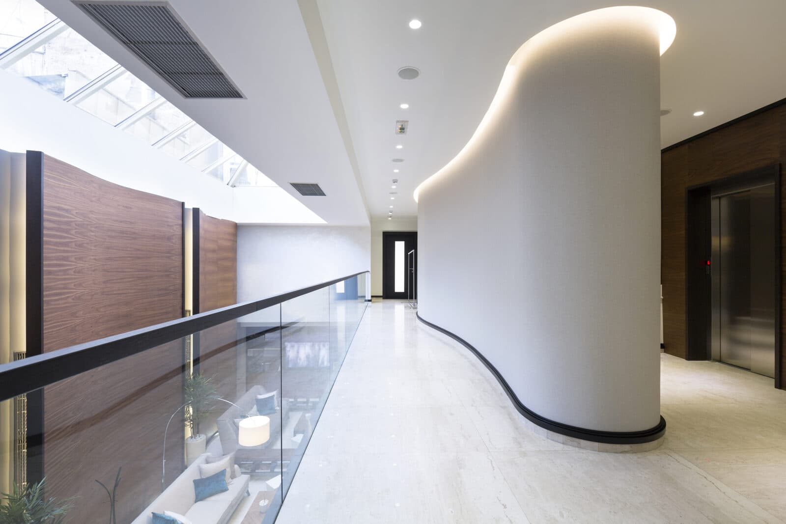 Curved commercial corridor lit by recessed downlights and LED cove lighting