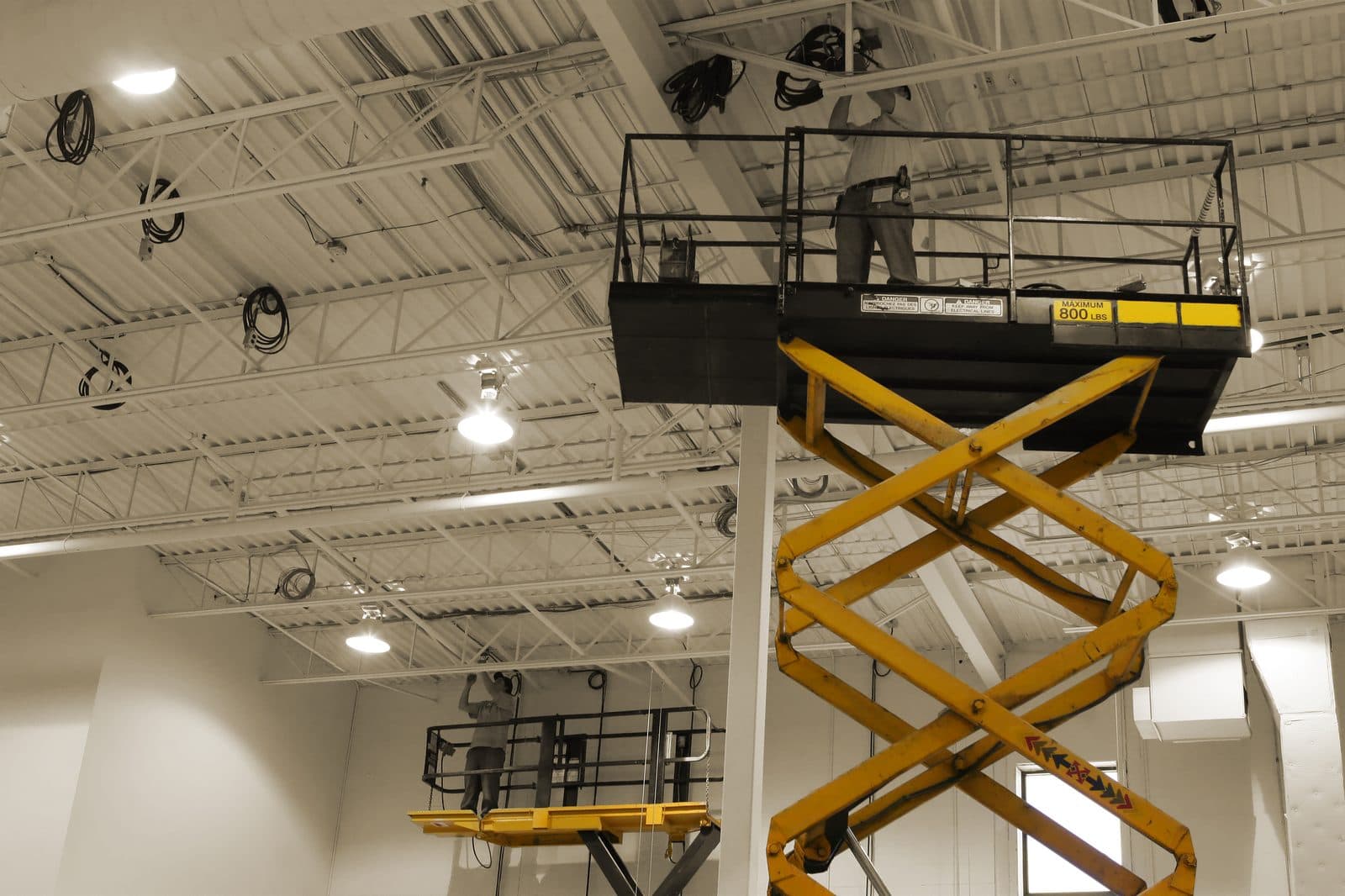 Electricians on scissor lifts installing overhead lighting in a commercial building